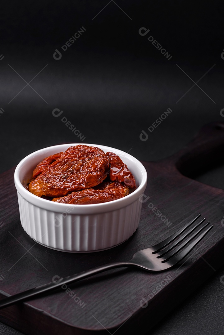 Deliciosos tomates secos ao sol em óleo numa tigela de cerâmica branca sobre um fundo escuro de concreto