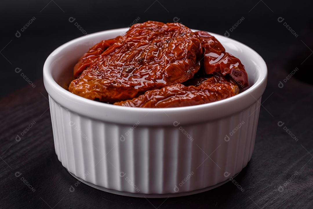 Deliciosos tomates secos ao sol em óleo numa tigela de cerâmica branca sobre um fundo escuro de concreto