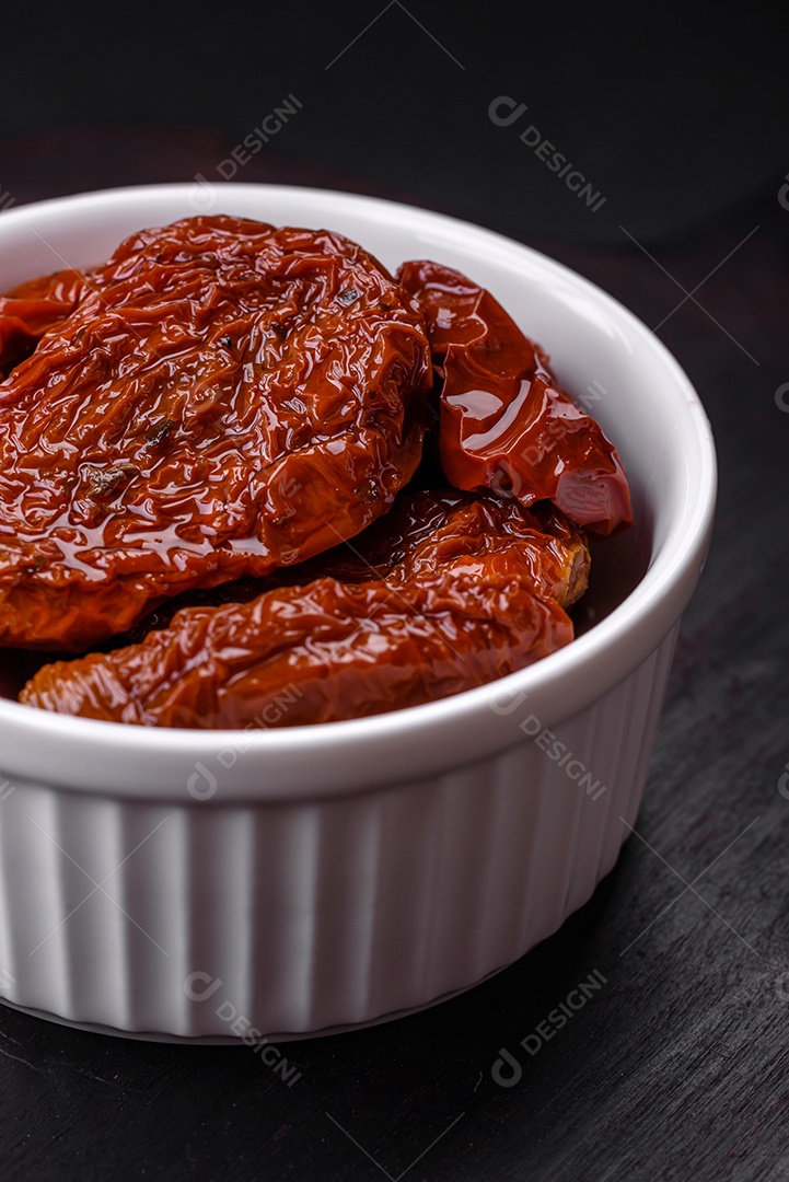 Deliciosos tomates secos ao sol em óleo numa tigela de cerâmica branca sobre um fundo escuro de concreto