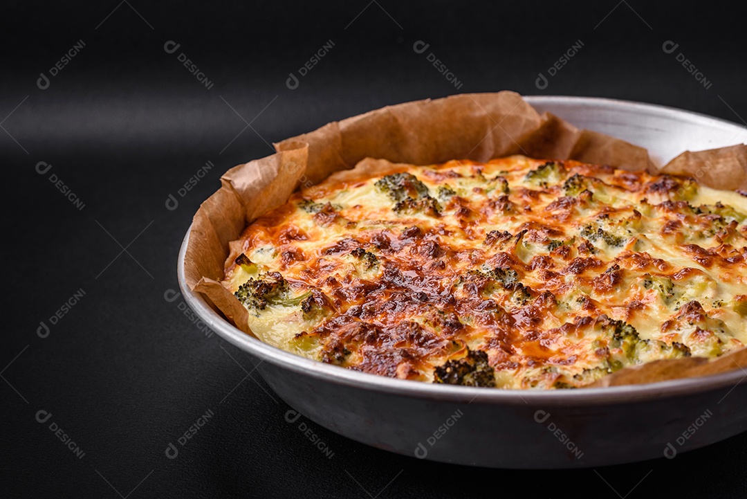 Deliciosa quiche com brócolis, queijo, frango, especiarias e ervas sobre um fundo escuro de concreto