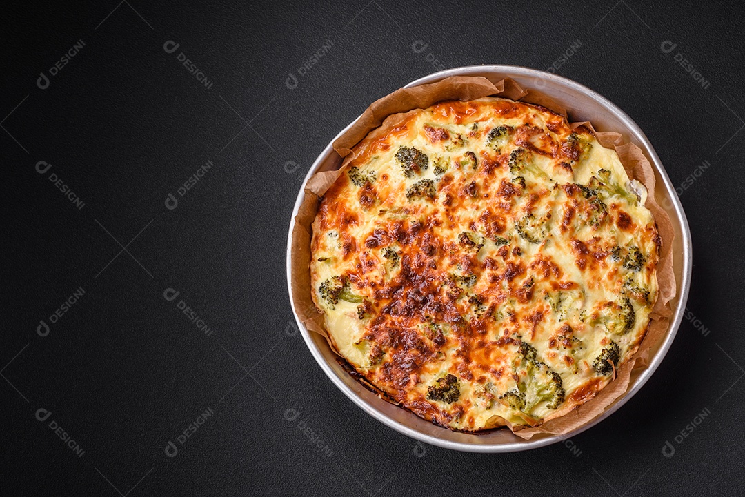Deliciosa quiche com brócolis, queijo, frango, especiarias e ervas sobre um fundo escuro de concreto