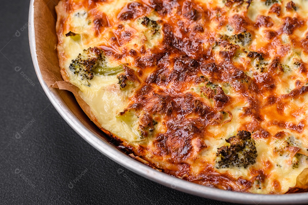 Deliciosa quiche com brócolis, queijo, frango, especiarias e ervas sobre um fundo escuro de concreto