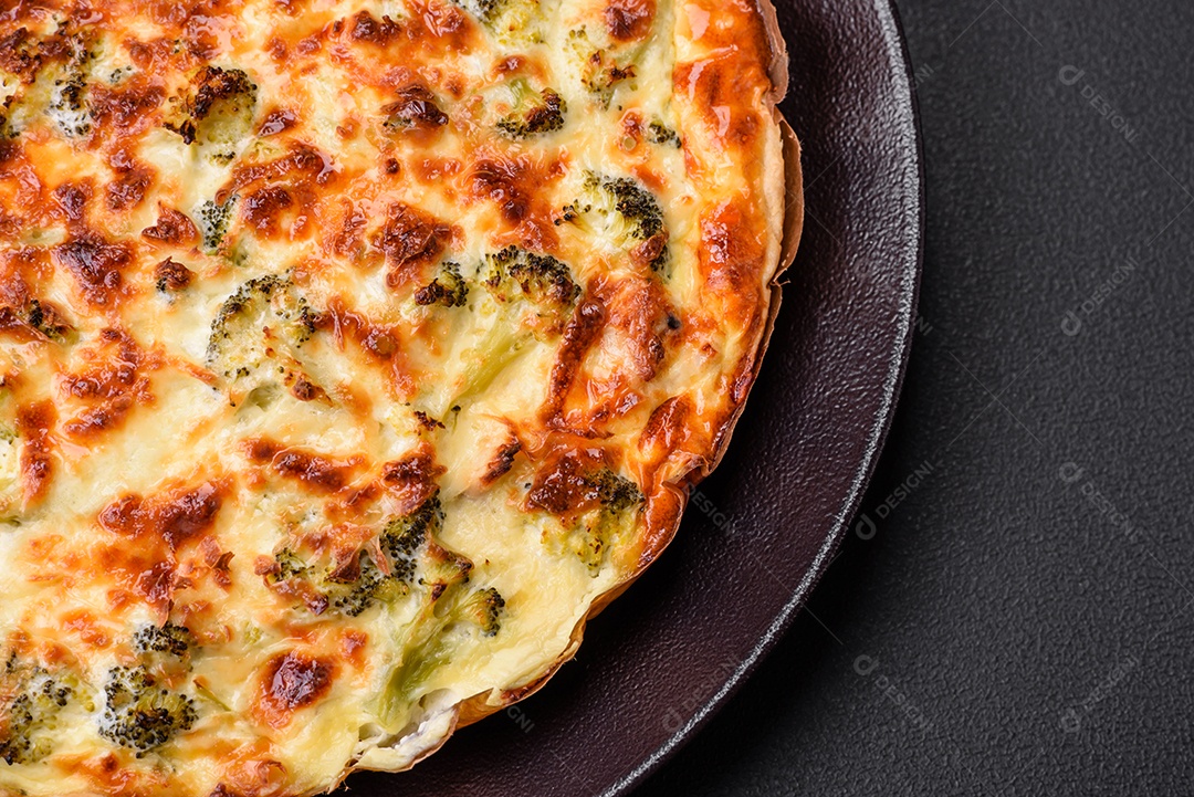 Deliciosa quiche com brócolis, queijo, frango, especiarias e ervas sobre um fundo escuro de concreto