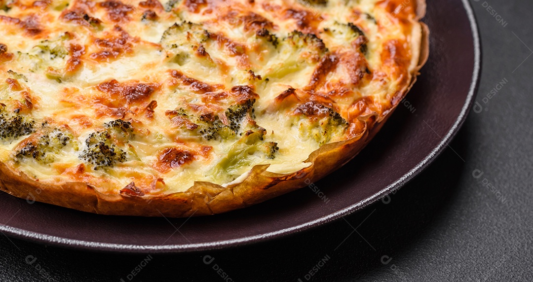 Deliciosa quiche com brócolis, queijo, frango, especiarias e ervas sobre um fundo escuro de concreto