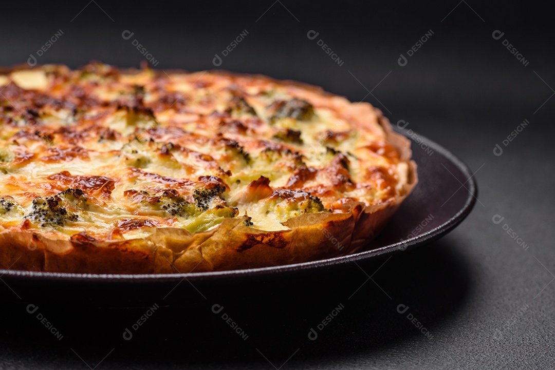 Deliciosa quiche com brócolis, queijo, frango, especiarias e ervas sobre um fundo escuro de concreto