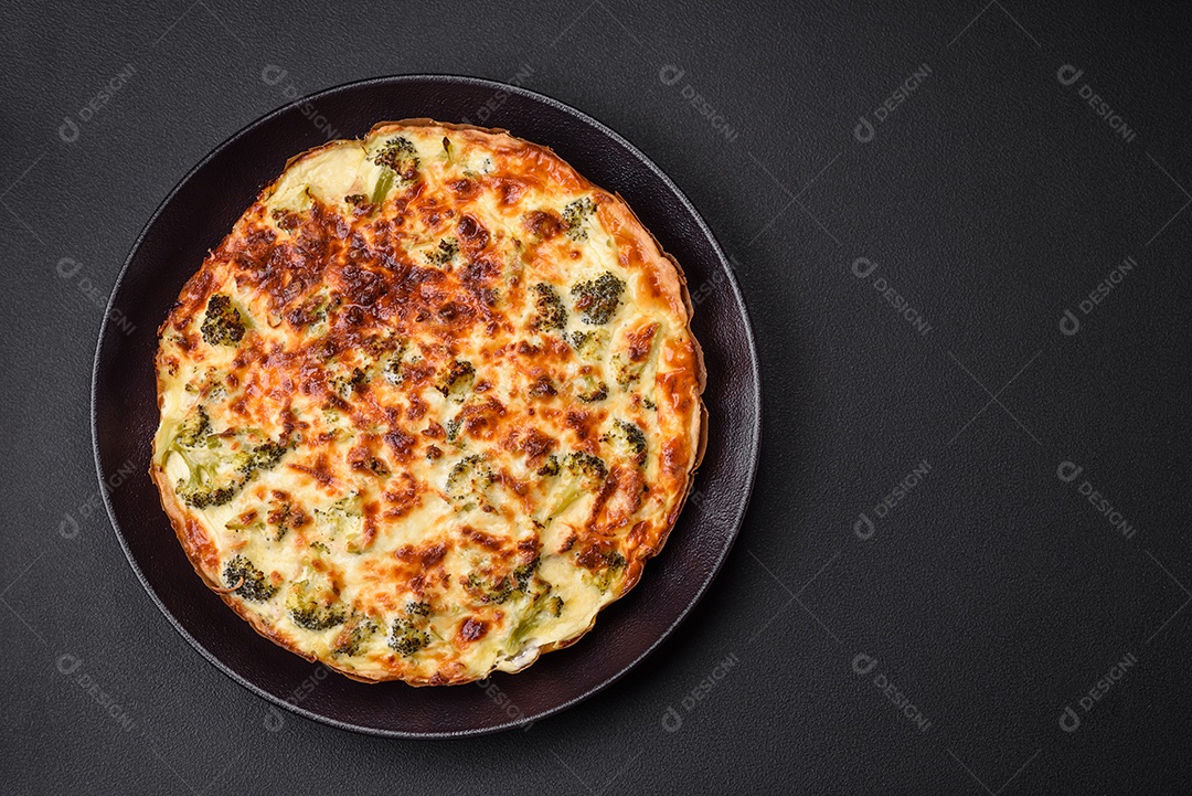 Deliciosa quiche com brócolis, queijo, frango, especiarias e ervas sobre um fundo escuro de concreto