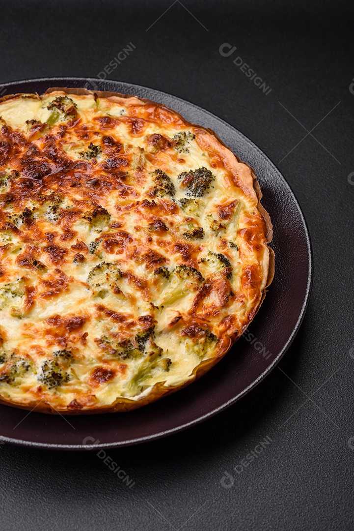 Deliciosa quiche com brócolis, queijo, frango, especiarias e ervas sobre um fundo escuro de concreto