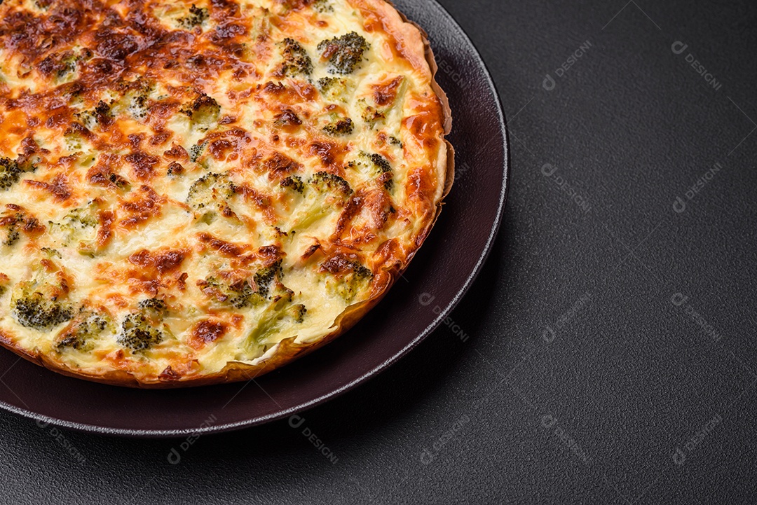 Deliciosa quiche com brócolis, queijo, frango, especiarias e ervas sobre um fundo escuro de concreto