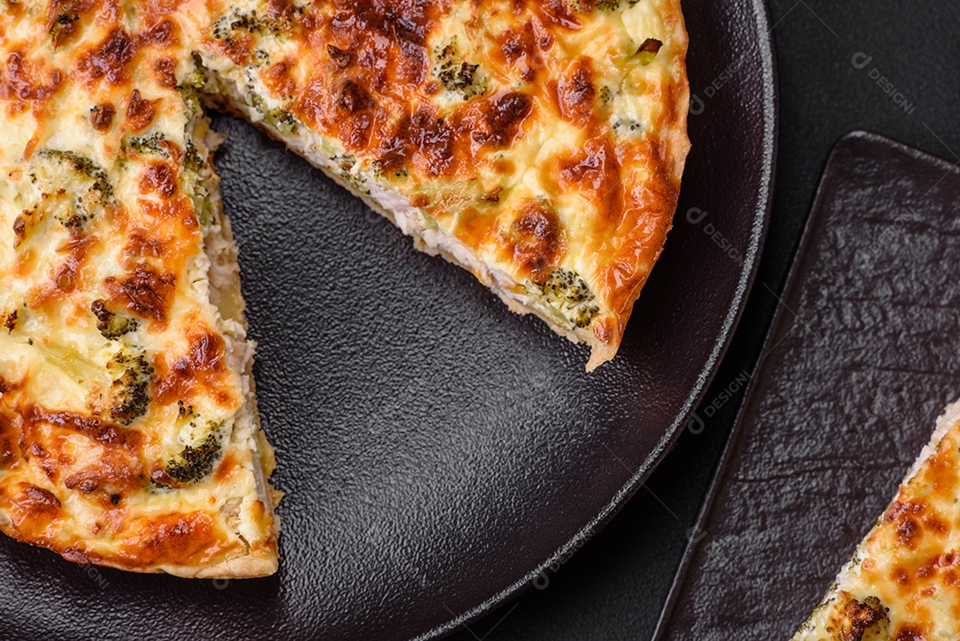 Deliciosa quiche com brócolis, queijo, frango, especiarias e ervas sobre um fundo escuro de concreto