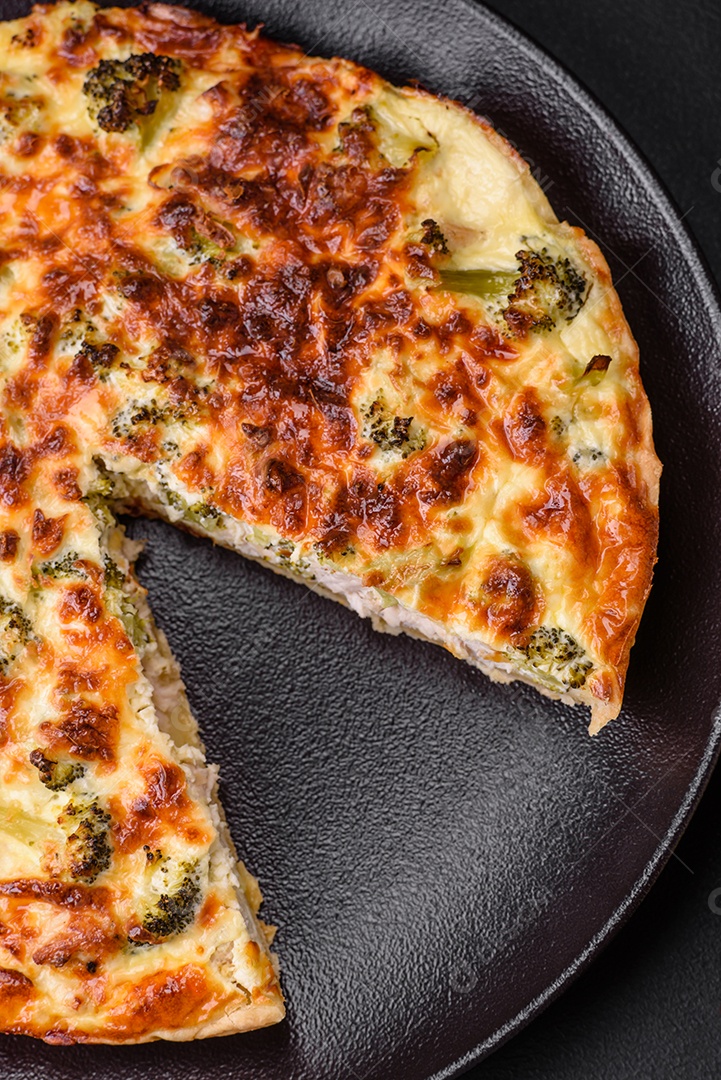 Deliciosa quiche com brócolis, queijo, frango, especiarias e ervas sobre um fundo escuro de concreto