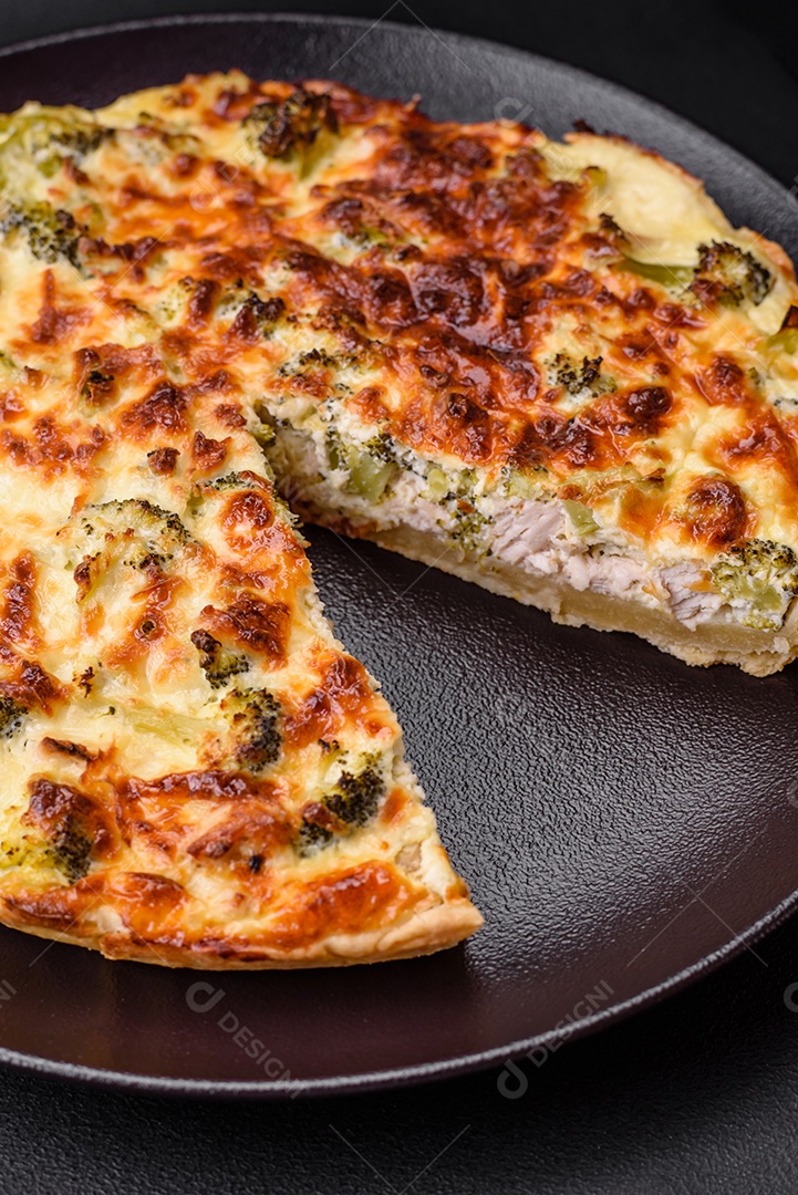 Deliciosa quiche com brócolis, queijo, frango, especiarias e ervas sobre um fundo escuro de concreto