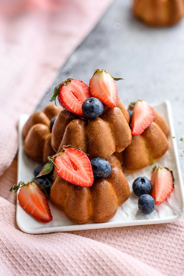 Deliciosos cupcakes ou muffins com passas e nozes, morangos e mirtilos num prato de cerâmica sobre uma mesa de concreto texturizado