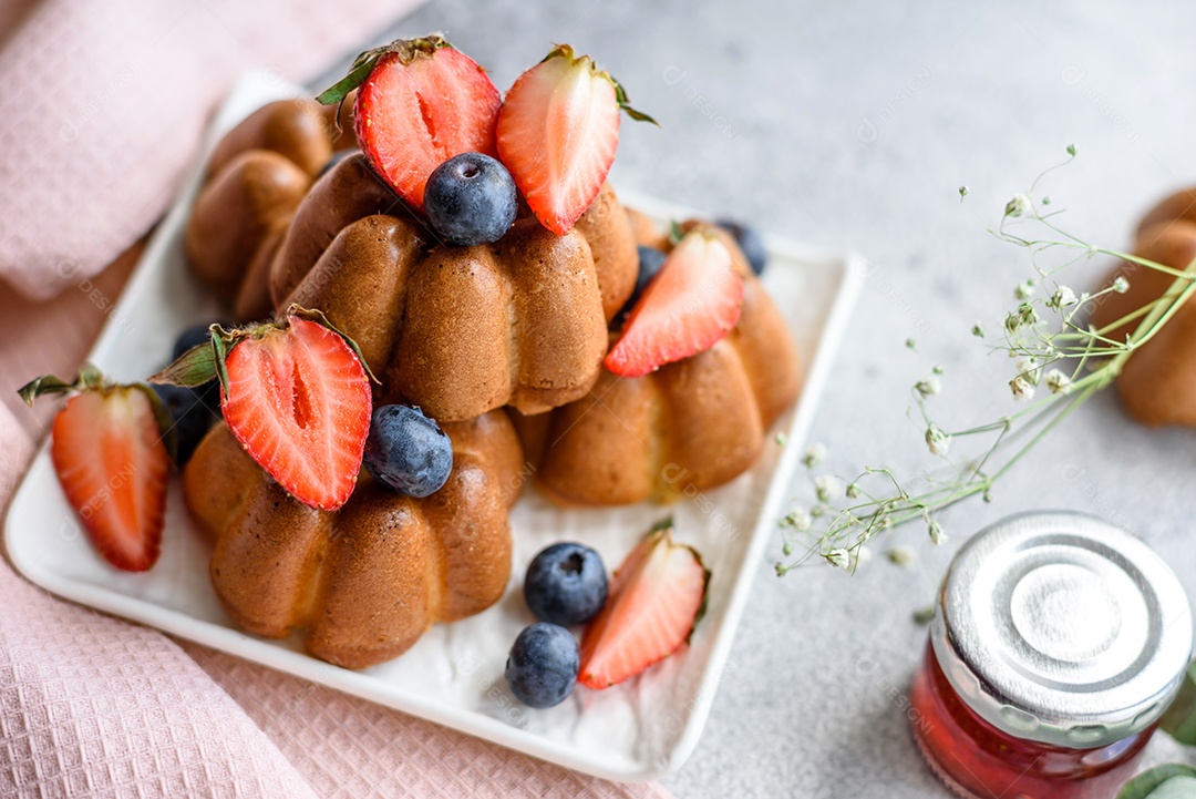 Deliciosos cupcakes ou muffins com passas e nozes, morangos e mirtilos num prato de cerâmica sobre uma mesa de concreto texturizado