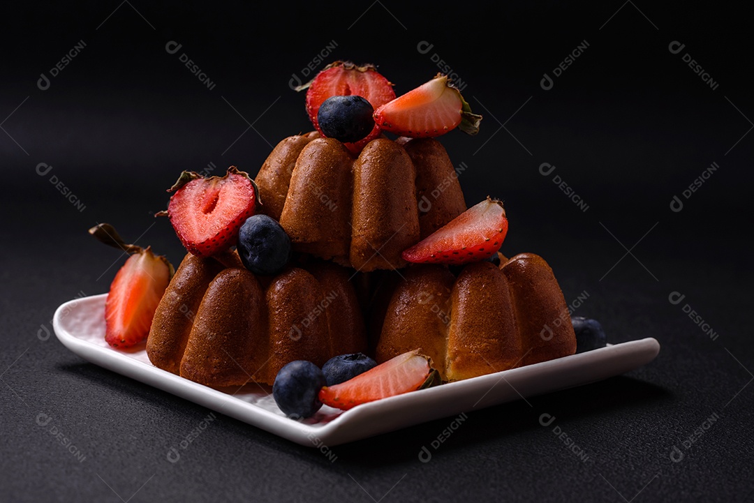 Deliciosos cupcakes ou muffins com passas e nozes, morangos e mirtilos num prato de cerâmica sobre uma mesa de concreto texturizado