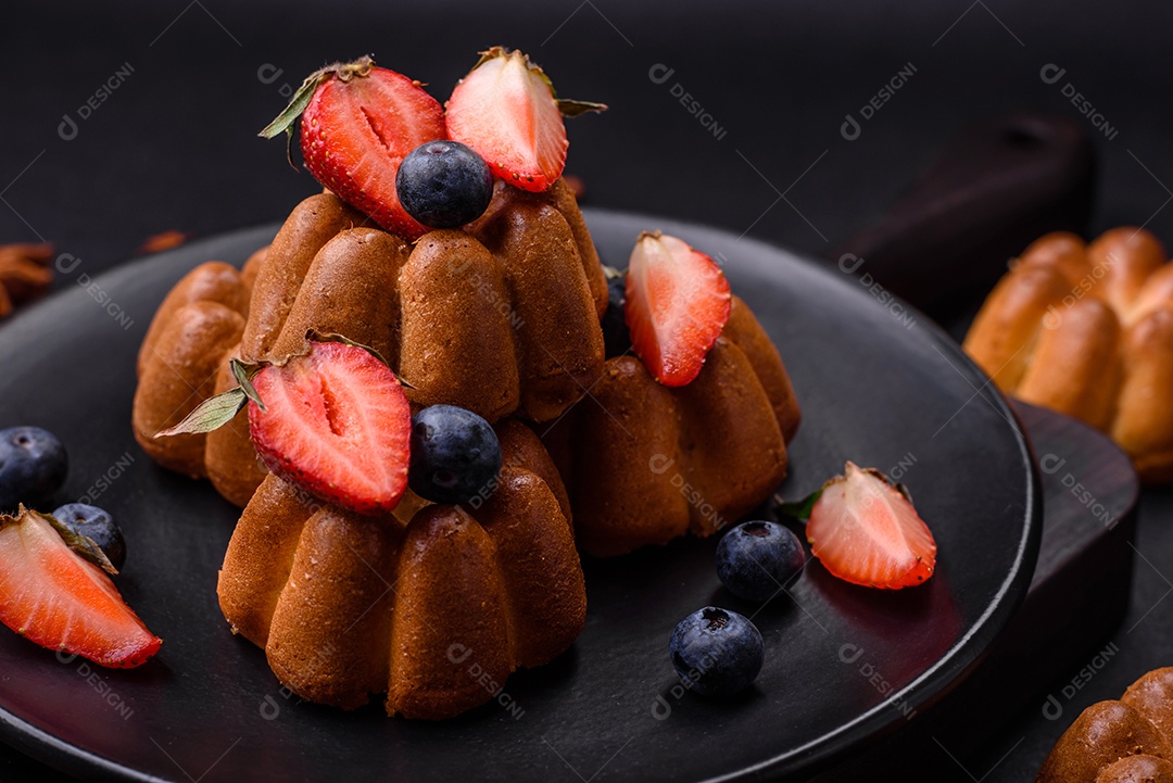 Deliciosos cupcakes ou muffins com passas e nozes, morangos e mirtilos num prato de cerâmica sobre uma mesa de concreto texturizado