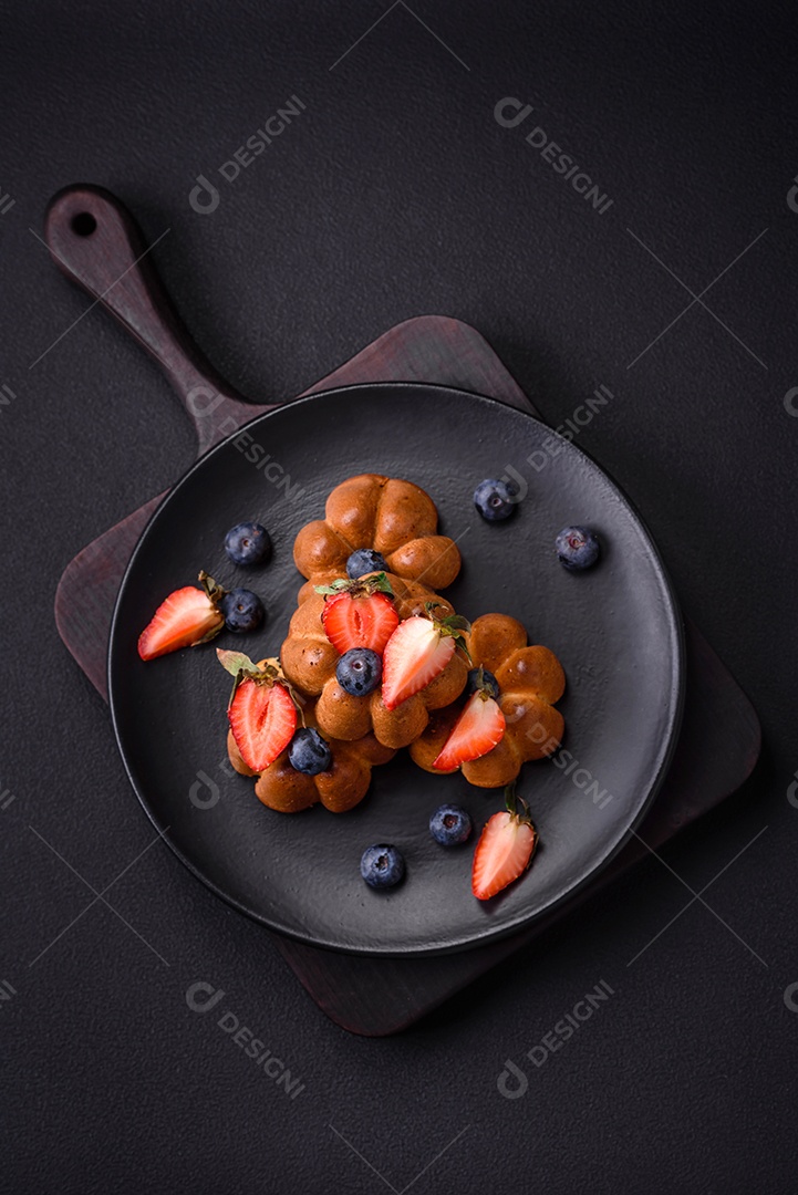 Deliciosos cupcakes ou muffins com passas e nozes, morangos e mirtilos num prato de cerâmica sobre uma mesa de concreto texturizado