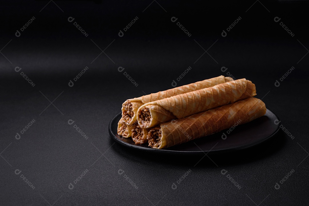 Deliciosos rolos de wafer crocante com recheio de creme com nozes em um fundo escuro de concreto