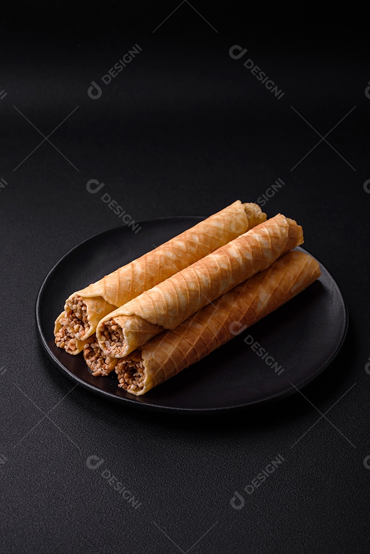 Deliciosos rolos de wafer crocante com recheio de creme com nozes em um fundo escuro de concreto