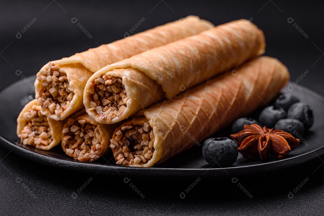 Deliciosos rolos de wafer crocante com recheio de creme com nozes em um fundo escuro de concreto