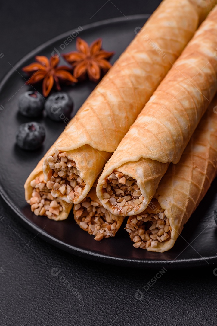 Deliciosos rolos de wafer crocante com recheio de creme com nozes em um fundo escuro de concreto