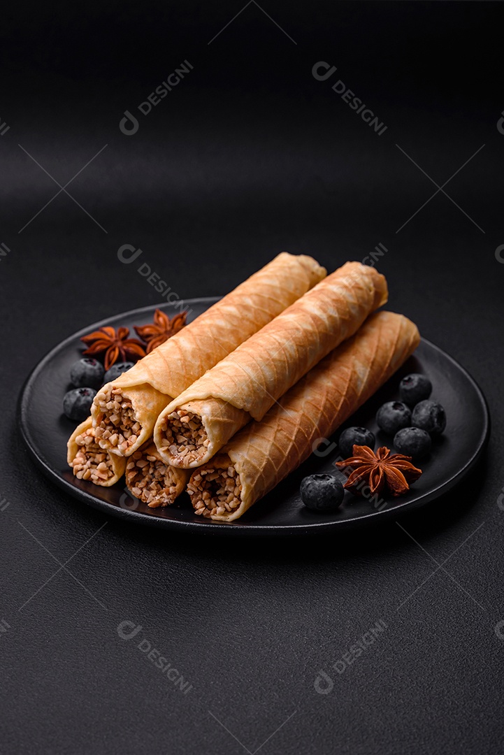 Deliciosos rolos de wafer crocante com recheio de creme com nozes em um fundo escuro de concreto