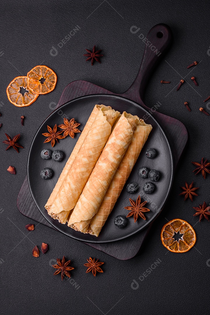 Deliciosos rolos de wafer crocante com recheio de creme com nozes em um fundo escuro de concreto