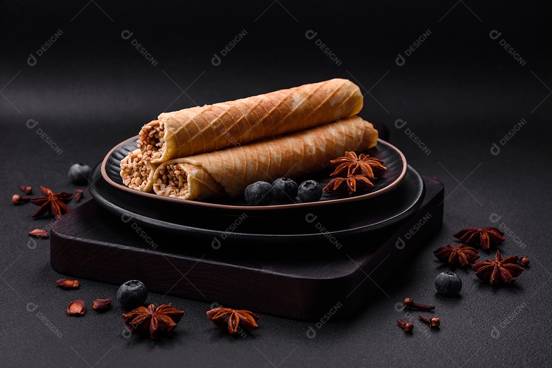 Deliciosos rolos de wafer crocante com recheio de creme com nozes em um fundo escuro de concreto