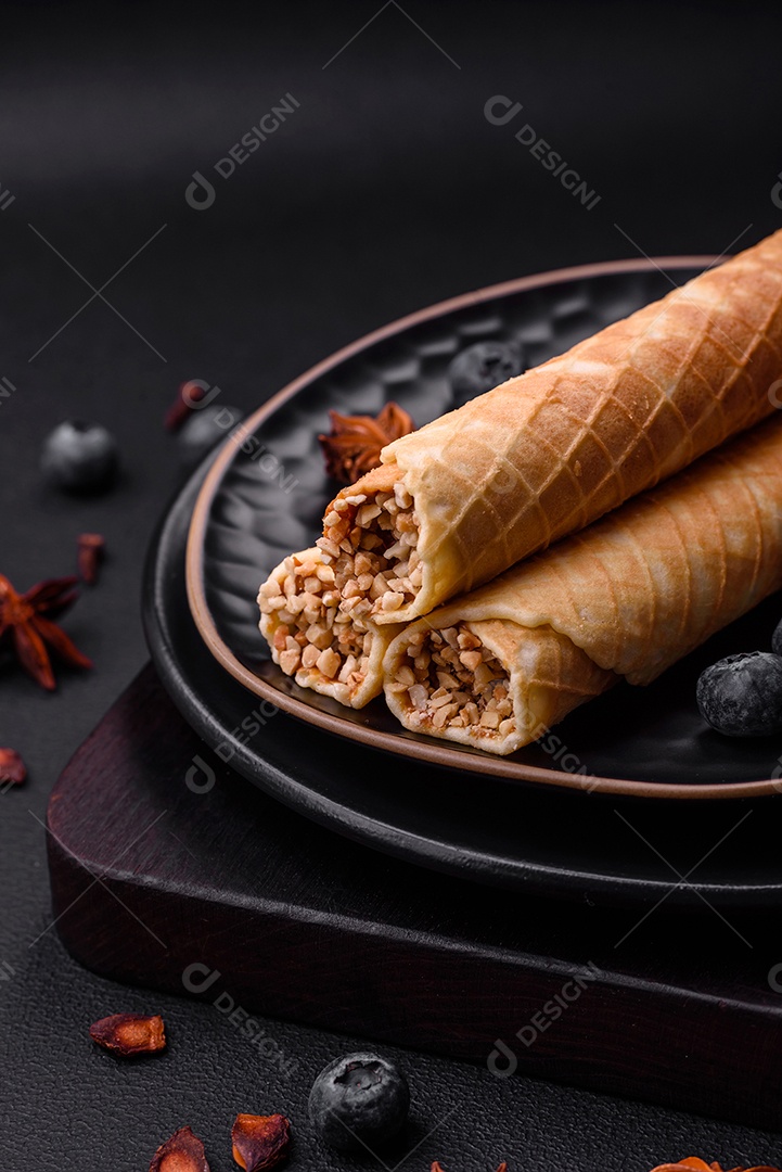 Deliciosos rolos de wafer crocante com recheio de creme com nozes em um fundo escuro de concreto