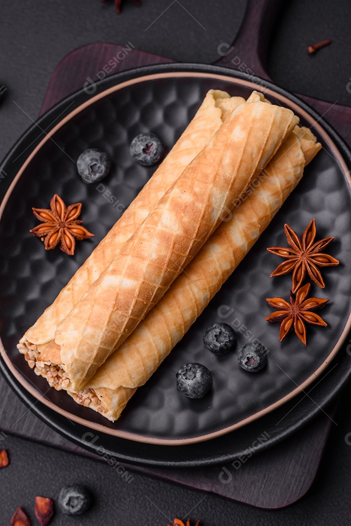 Deliciosos rolos de wafer crocante com recheio de creme com nozes em um fundo escuro de concreto