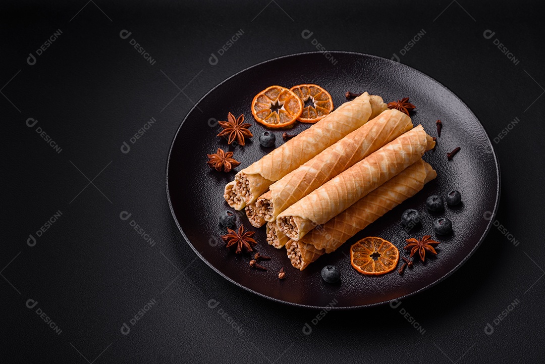 Deliciosos rolos de wafer crocante com recheio de creme com nozes em um fundo escuro de concreto