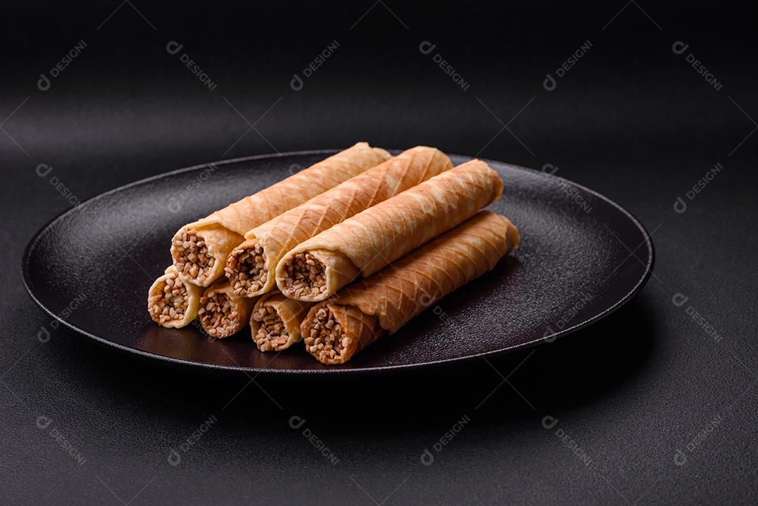 Deliciosos rolos de wafer crocante com recheio de creme com nozes em um fundo escuro de concreto