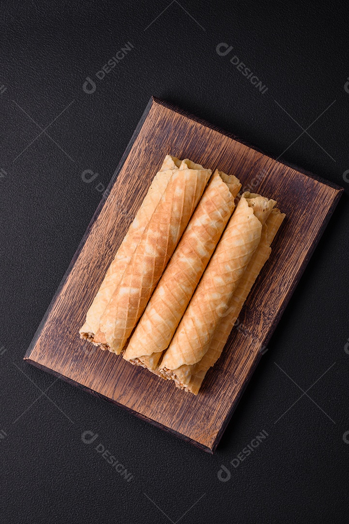 Deliciosos rolos de wafer crocante com recheio de creme com nozes em um fundo escuro de concreto