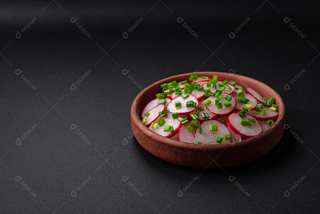 Deliciosa salada fresca de rabanetes fatiados com cebolinha, sal e azeite sobre um fundo escuro de concreto