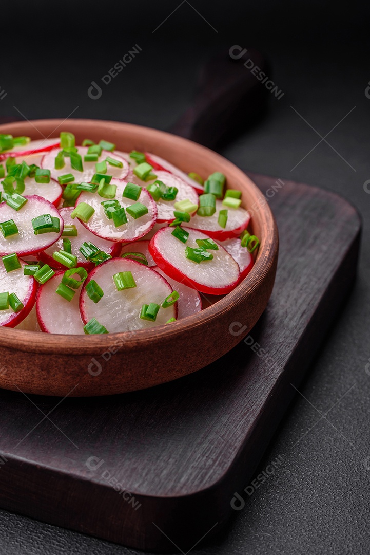 Deliciosa salada fresca de rabanetes fatiados com cebolinha, sal e azeite sobre um fundo escuro de concreto