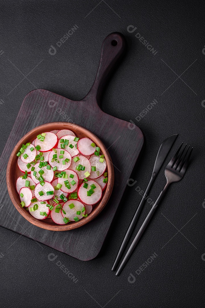 Deliciosa salada fresca de rabanetes fatiados com cebolinha, sal e azeite sobre um fundo escuro de concreto