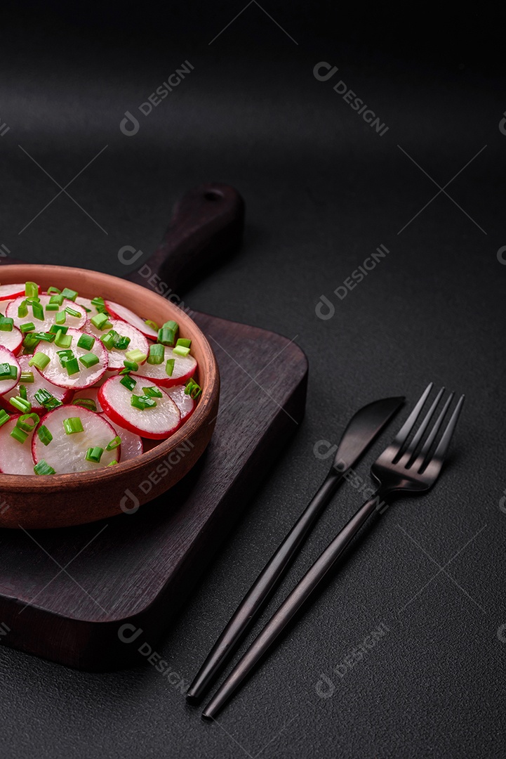 Deliciosa salada fresca de rabanetes fatiados com cebolinha, sal e azeite sobre um fundo escuro de concreto