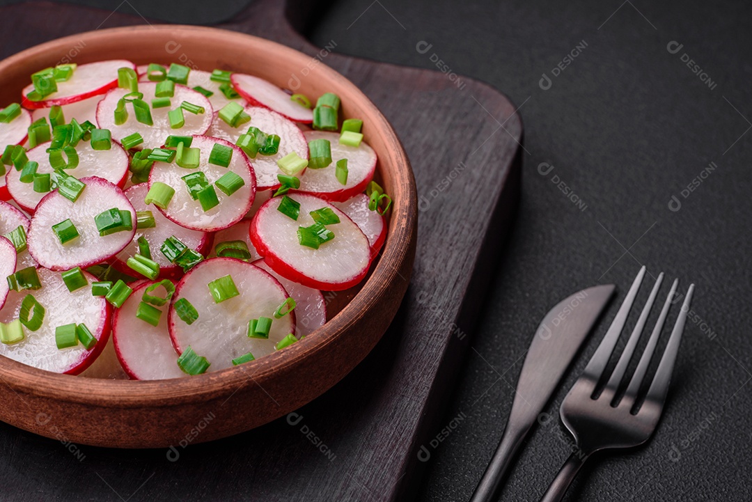 Deliciosa salada fresca de rabanetes fatiados com cebolinha, sal e azeite sobre um fundo escuro de concreto