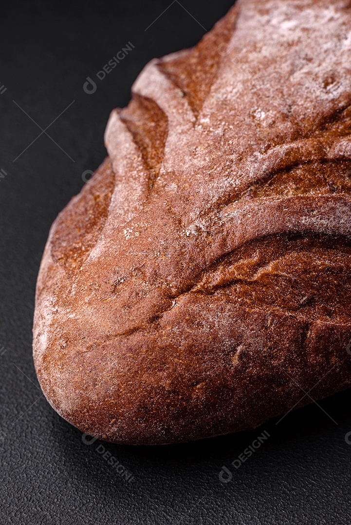 Delicioso pão integral crocante fresco com grãos de cereais e especiarias sobre um fundo escuro de concreto