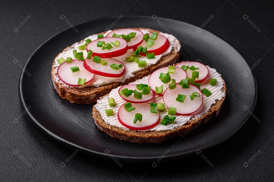 Delicioso sanduíche ou bruscheta com rabanete de cream cheese e cebolinha sobre um fundo escuro de concreto