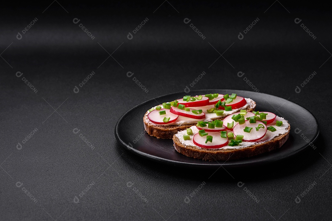 Delicioso sanduíche ou bruscheta com rabanete de cream cheese e cebolinha sobre um fundo escuro de concreto