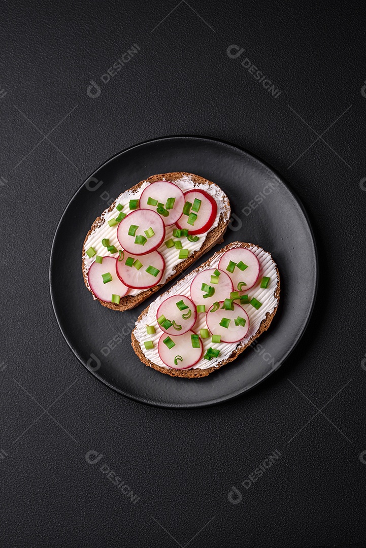 Delicioso sanduíche ou bruscheta com rabanete de cream cheese e cebolinha sobre um fundo escuro de concreto