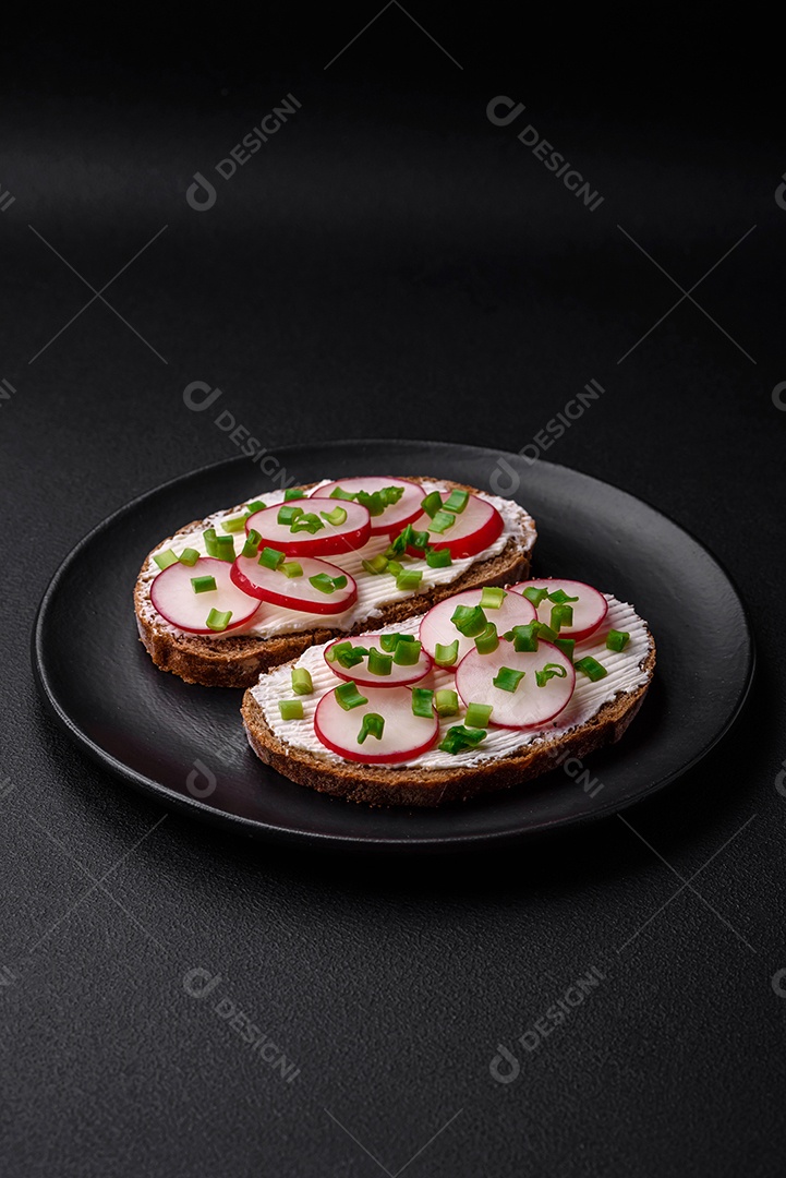 Delicioso sanduíche ou bruscheta com rabanete de cream cheese e cebolinha sobre um fundo escuro de concreto