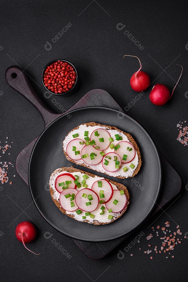 Delicioso sanduíche ou bruscheta com rabanete de cream cheese e cebolinha sobre um fundo escuro de concreto