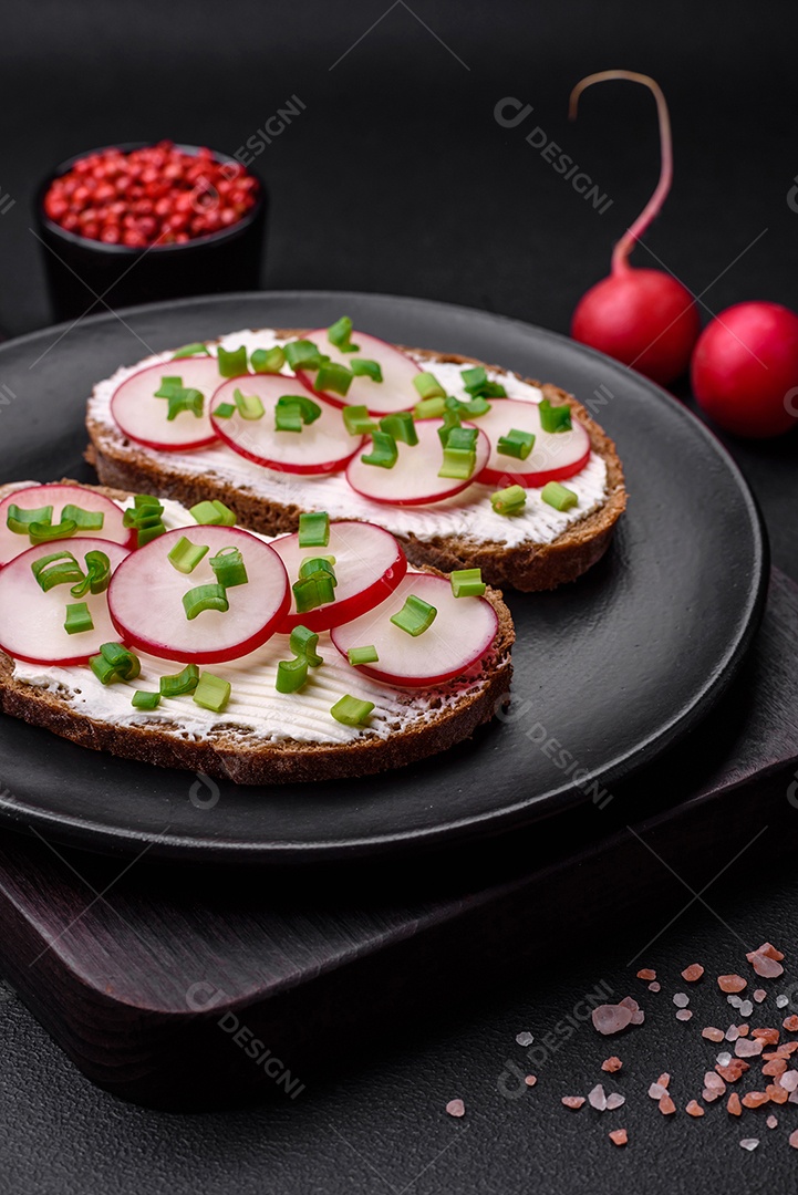 Delicioso sanduíche ou bruscheta com rabanete de cream cheese e cebolinha sobre um fundo escuro de concreto