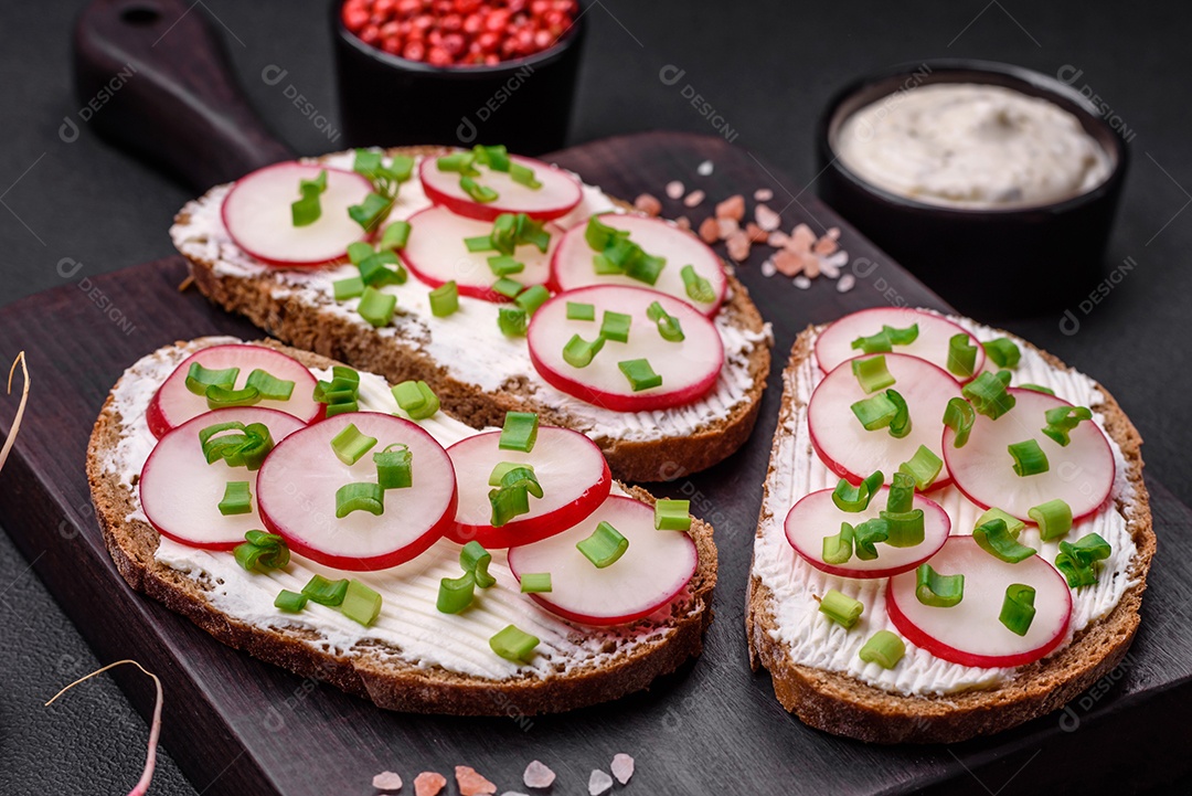 Delicioso sanduíche ou bruscheta com rabanete de cream cheese e cebolinha sobre um fundo escuro de concreto