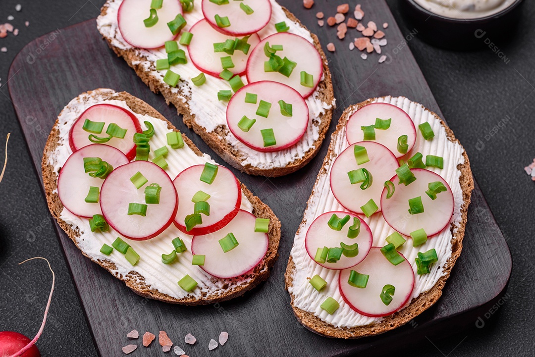 Delicioso sanduíche ou bruscheta com rabanete de cream cheese e cebolinha sobre um fundo escuro de concreto