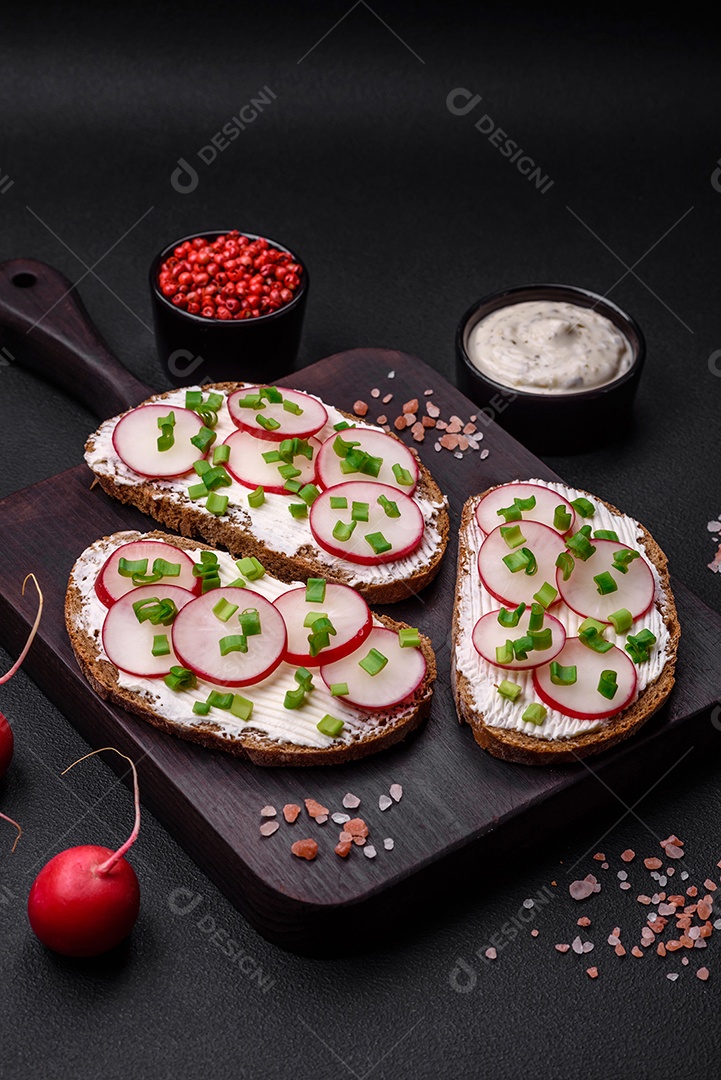 Delicioso sanduíche ou bruscheta com rabanete de cream cheese e cebolinha sobre um fundo escuro de concreto