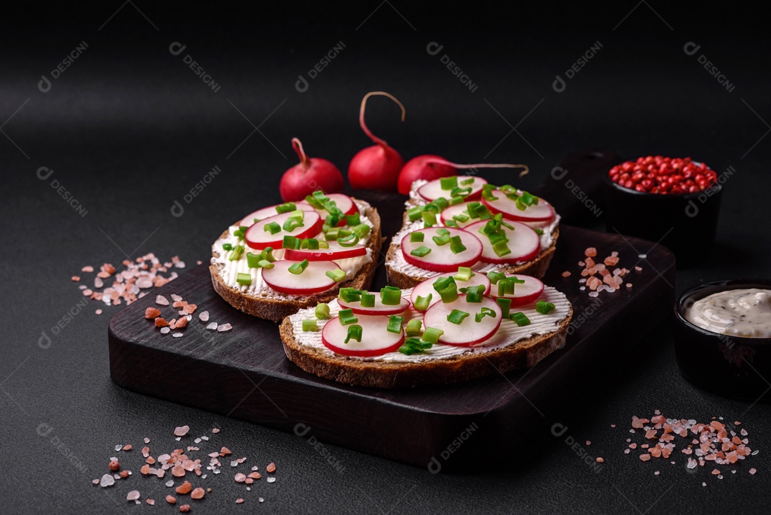 Delicioso sanduíche ou bruscheta com rabanete de cream cheese e cebolinha sobre um fundo escuro de concreto