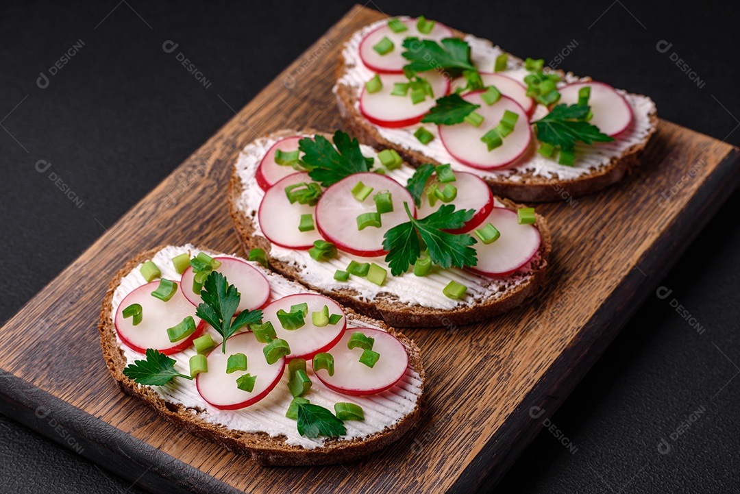 Delicioso sanduíche ou bruscheta com rabanete de cream cheese e cebolinha sobre um fundo escuro de concreto