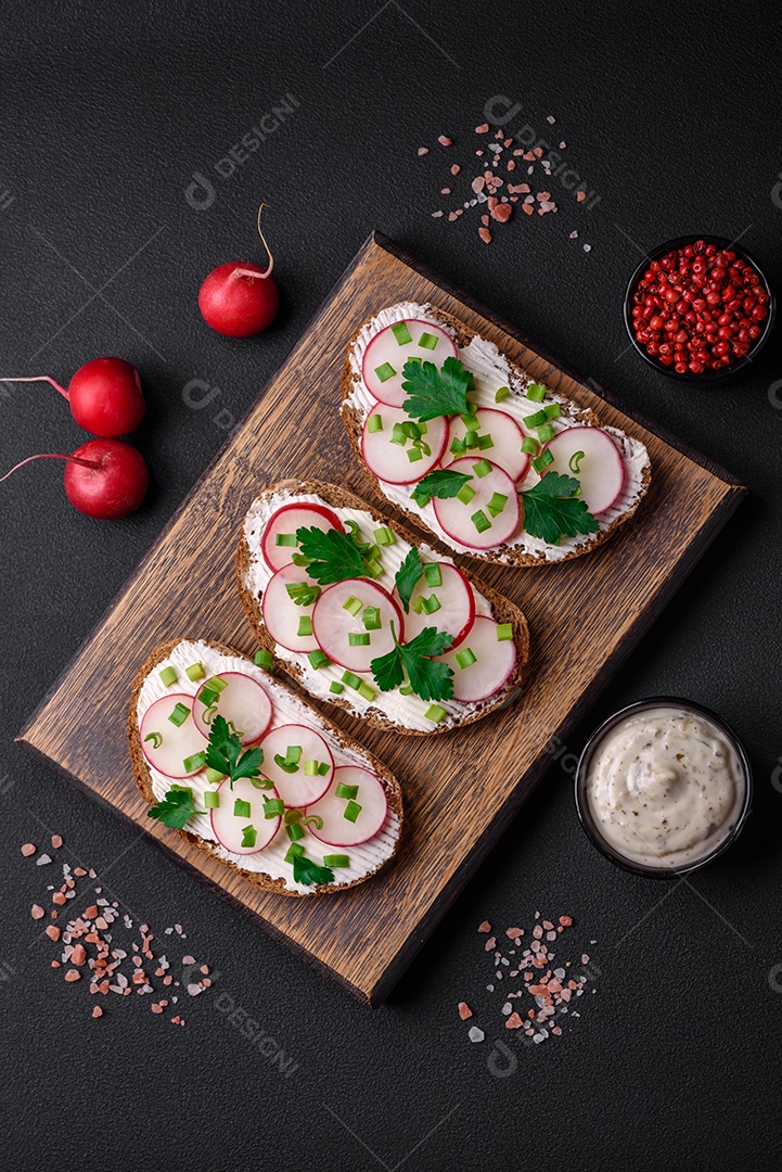 Delicioso sanduíche ou bruscheta com rabanete de cream cheese e cebolinha sobre um fundo escuro de concreto